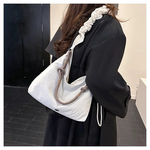 Detail of white fabric hobo bag featuring a ruffled strap and dark brown rope knot decoration