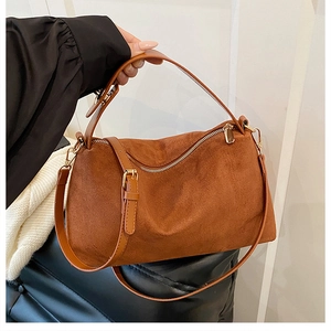 Close-up of brown suede shoulder bag with gold hardware and curved zipper design