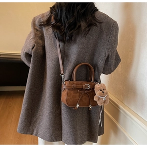 Brown suede crossbody bag detail featuring a pearl-decorated plush bear charm and ribbon