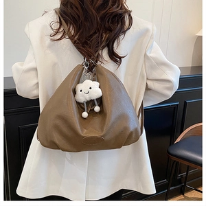Detail of dark brown leather hobo bag with plush cloud charm on a white blazer model