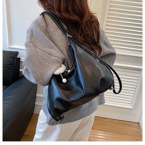 Detail of black faux leather tote bag with plush charm and side fashion label