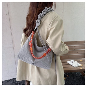 Detail of grey crossbody bag featuring orange rope decor and pleated shoulder strap