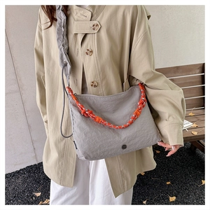 Detail of light gray nylon crossbody bag with pleated strap and orange woven handle