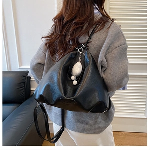 Close-up of black pleated faux leather backpack featuring a plush white charm pendant