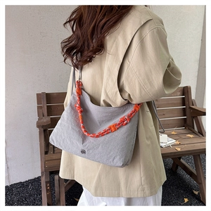 Detail of grey nylon crescent hobo bag featuring a vibrant woven orange and blue strap