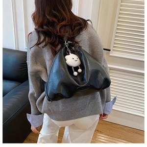 Detail of black PU leather shoulder bag featuring a white plush cloud charm on a strap