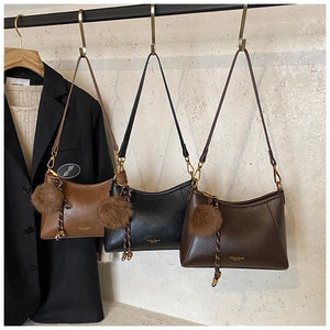 Three stylish crossbody dumpling bags in tan, black and dark brown with pompom charms