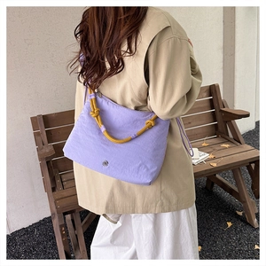 Detail of lavender nylon shoulder bag with yellow rope handle on outdoor wooden bench