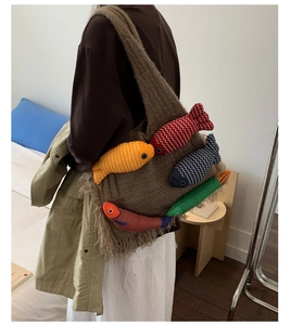 Detail of a brown knit tote bag featuring colorful fish plush charms and fringe tassels