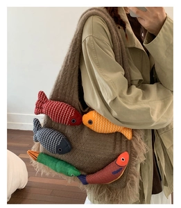Detail of a brown knit tote bag featuring colorful plush fish charms and long fringe tassels