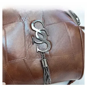 Detail der braunen Umhängetasche mit silbernem S-Logo und metallischer Quaste