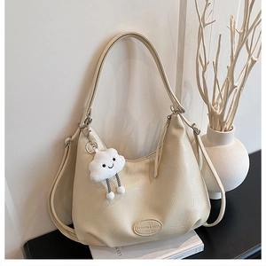 Detail of beige crescent shoulder bag with plush cloud charm and embossed fashion text
