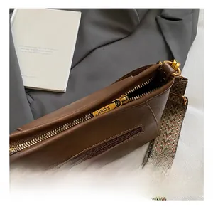 Detail of brown leather crossbody bag with golden zipper and wavy woven shoulder strap