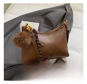 Detail of brown PU leather hobo bag featuring woven strap and soft plush ball charm
