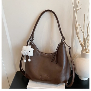 Detail of dark brown hobo bag on books with white cloud plush charm and metal zipper pull