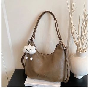 Detail of a brown vintage crescent bag with plush cloud charm on a stack of books
