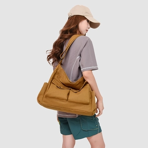 Détail du grand sac bandoulière en toile marron avec poches à rabat sur le mannequin