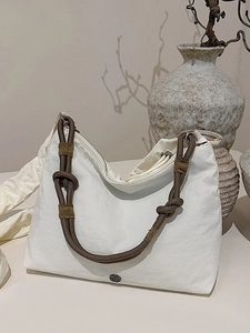 White canvas crossbody bag with decorative brown rope knot shoulder strap in a minimalist style