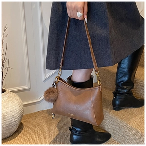 Detailed view of a brown faux leather shoulder bag with a plush ball charm on a staircase