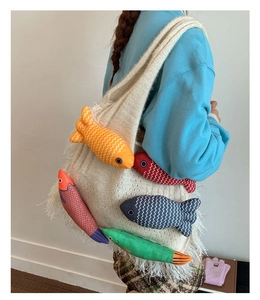 Detail of beige knitted tote bag featuring colorful fish plush charms and white fringe edges