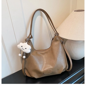 Close-up of tan leather shoulder bag with lychee texture and cloud plush charm detail