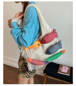 Detail of knitted tote bag featuring colorful plush fish charms and white fringe trim