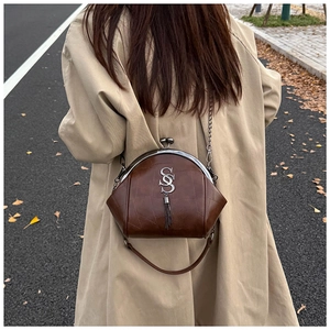 Details einer braunen Leder-Arzttasche mit Metallverschluss und Quaste am schicken Trenchcoat