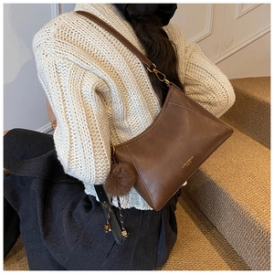 Close-up of retro brown leather shoulder bag with gold logo and plush ball accessory