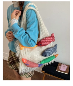 Detail view of cream knit tote bag featuring colorful fish plush charms and long white fringe