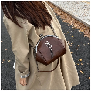 Detail der Vintage-Umhängetasche mit Metallquaste auf beigem Trenchcoat-Outfit