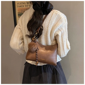 Close-up of brown PU leather shoulder bag featuring a fuzzy pom-pom and braided strap
