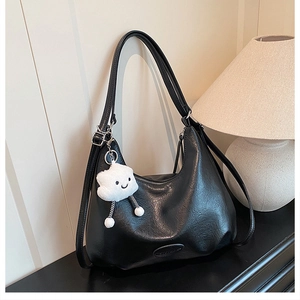 Close-up of black PU hobo bag with a white plush cloud charm in a cozy indoor setting