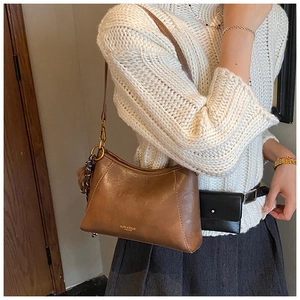 Brown leather crossbody bag with gold logo and pom-pom charm on grey skirt style