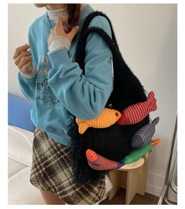 Detail of a black fuzzy tote bag featuring colorful stuffed fish charms worn by a model