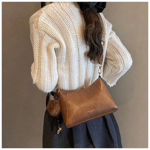 Brown vintage dumpling bag with metal buckle and plush pom-pom charm shown on a model