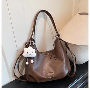 Detail of dark brown leather bag with embossed text and white cloud plush charm accessory