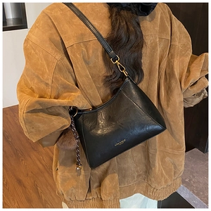 Detail of black leather crescent bag with golden logo and brown fur ball pendant