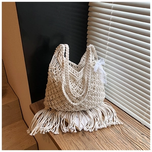Detail of hand-woven mesh beach tote with long fringes and white lace bow decoration