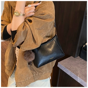 Detailed view of black trapezoid shoulder bag with leather texture and plush charm