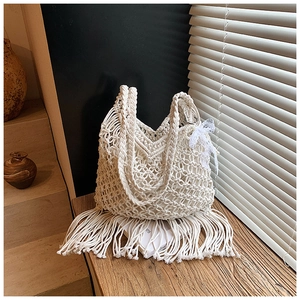 Detail of white macrame hand-woven tote bag featuring long fringes and lace bow decoration