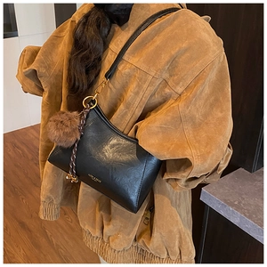Detail of black leather crossbody bag with golden hardware and fuzzy pompom charm