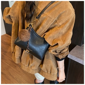 Close-up of black leather crossbody bag with gold logo and brown plush charm accessory