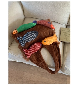 Detail of a brown knit tote bag featuring colorful hanging fish dolls and decorative fringe