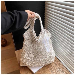 Close-up of white crochet tote bag with lace bow and pearl charm against wood background