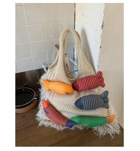 Detail of beige knitted tote bag featuring colorful fabric fish charms and long bottom tassels