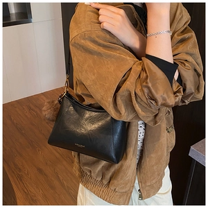 Detail view of black matte leather shoulder bag with gold logo and brown plush charm