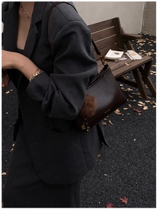 Detail of dark brown leather crossbody bag with fluffy charm and gold branding