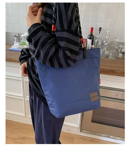 Dettaglio della borsa tote a scacchi blu con tracolla intrecciata e logo in pelle su sfondo moderno