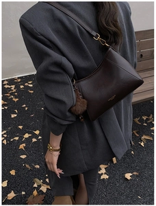 Detail of dark brown leather crossbody bag with fluffy charm and gold buckle on strap
