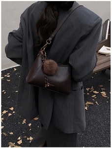 Detail of dark brown leather crescent bag with gold logo and plush pompom charm decoration